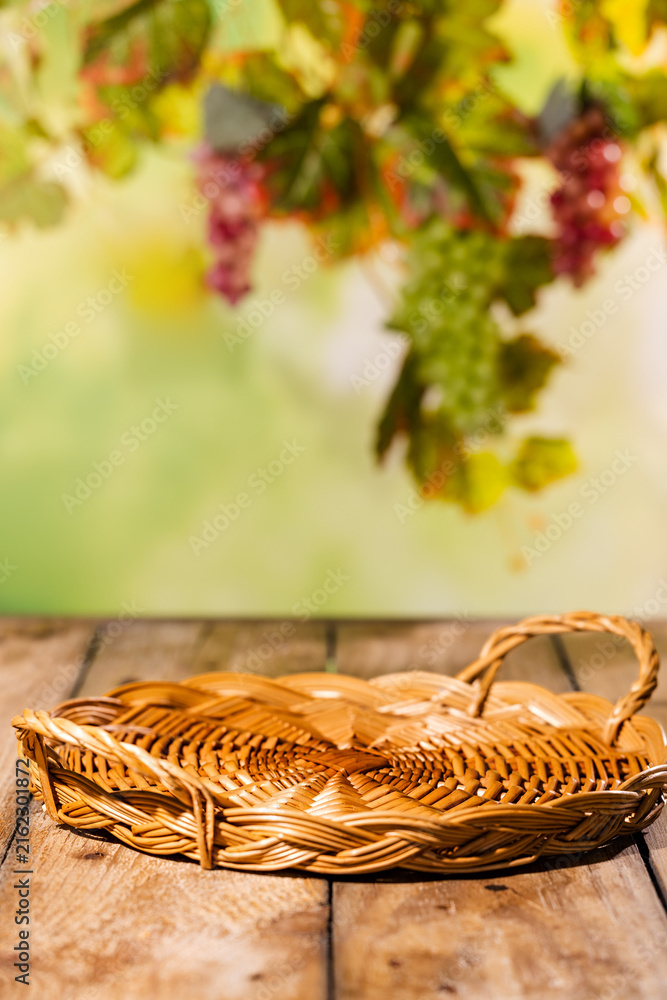 Naklejka premium Low wicker tray on rustic wooden table with blurred grapevine background for autumn harvest product mockup