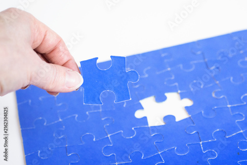 Quadro su tela Hand placing last  puzzle piece in blue jigsaw, completion concept, close up