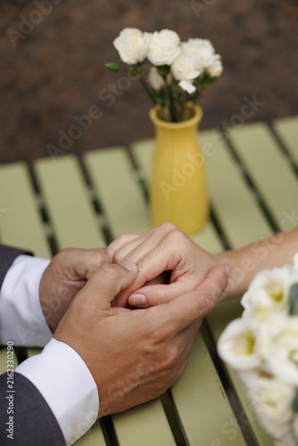 Groom holds bride hands gently at outdoor table with white roses