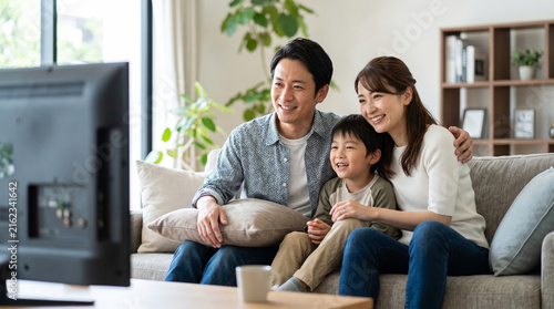 リビングのソファで仲良くテレビを見る笑顔の3人家族