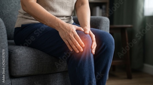 Person sitting on a sofa holding their knee with a red glow effect symbolizing joint pain and inflammation