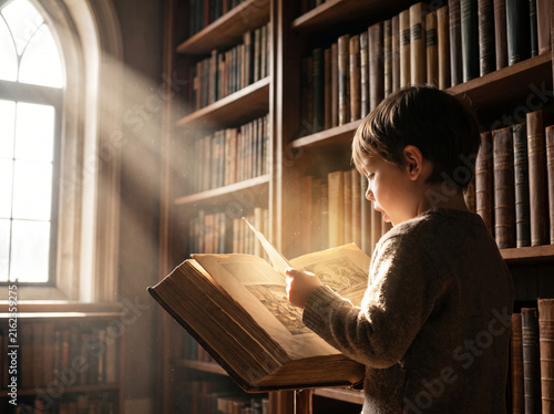 Young boy reading a large glowing book in a classic library with sunlight.