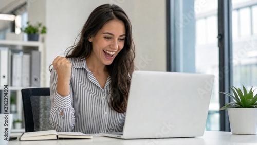 Excited businesswoman celebrating success at her office desk with a laptop computer.