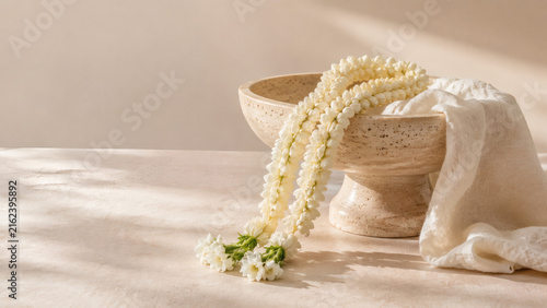 Sampaguita flower garland draped over a travertine bowl with linen fabric in a minimalist natural still life setting
