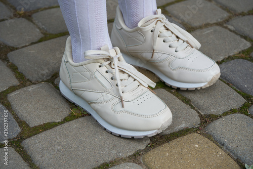 Beige leather sneakers on a girl's feet, Close-up of cream color running shoes and white socks outdoor feet standing on paving stone pavement