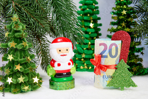 A euro banknote with decorations and Santa Claus among green Christmas trees