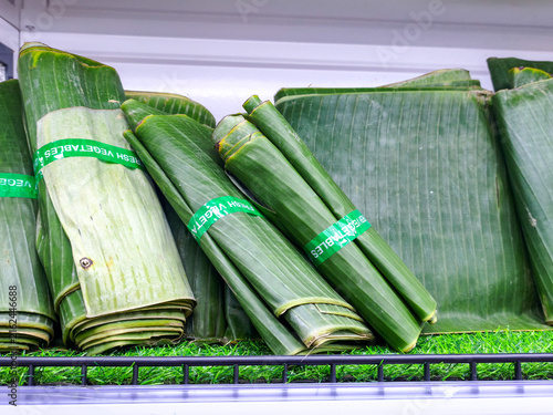 Bundles of Fresh Green Banana Leaves. Premium folded green banana leaves bundled with produce tape on display in a grocery refrigerator shelf, ideal for traditional steaming and wrapping food.