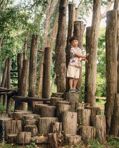 Bild auf Leinwand A young child exploring and climbing a natural wooden playground surrounded by trees, enjoying outdoor adventure, physical activity, and imaginative play in nature