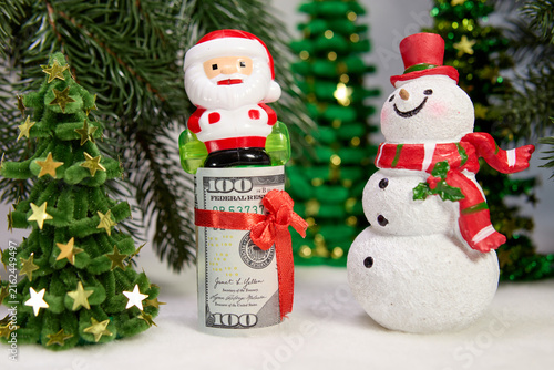 A dollar bill with a red ball and Santa Claus among green Christmas trees