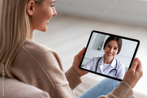 Young woman using tablet for telemedicine video call consultation with female doctor at home.