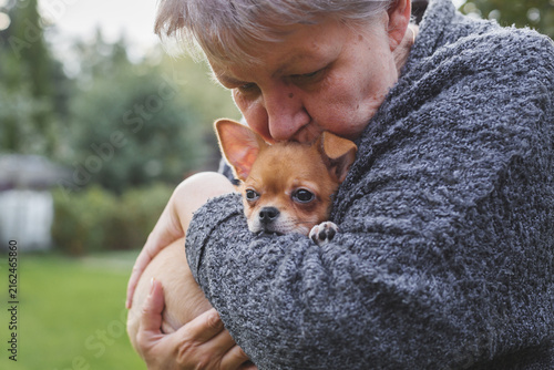 Konstfotografi Elderly woman tenderly hugging and kissing a small chihuahua puppy outdoors, con