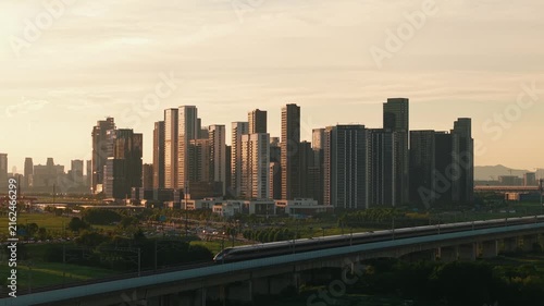 Aerial view of a high speed train travels on an elevated track past tall apartment buildings in a city suburb during sunset in China