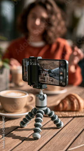 Smartphone on Mini Flexible Tripod Recording Young Woman Having Breakfast at Outdoor Cafe Table