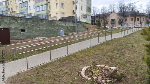 In order for people with disabilities to move around the city block, an inclined ramp made of tiles with metal railings was made. Barrier-free environment. There are buildings and trees nearby. Cloudy