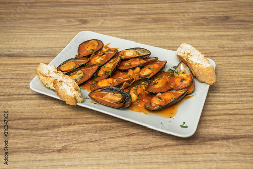Mussels in Spicy Tomato Sauce with Toasted Bread Slices on Rectangular White Plate
