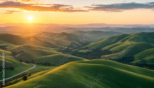 Rolling green hills illuminated by a golden sunset in a peaceful mountain landscape.