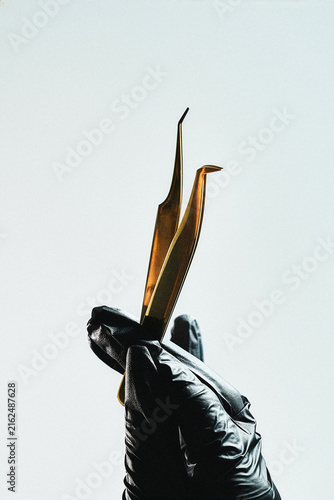 Gold lash tweezers open in a V-shape, close-up on light background