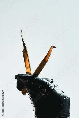 Gold eyelash tweezers held by a lash technician, close-up