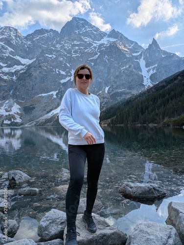 Obraz na płótnie Young woman hiker standing on rocks by scenic alpine mountain lake Morskie Oko i