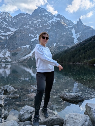 Foto Young woman hiker standing on rocks by scenic alpine mountain lake Morskie Oko i