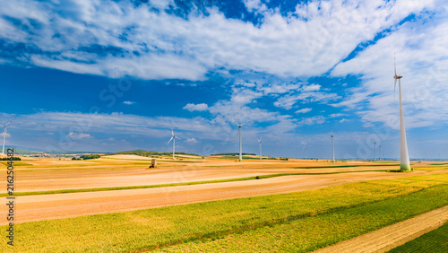 Obraz na plátně Wind turbines stand in open fields under blue sky with clouds