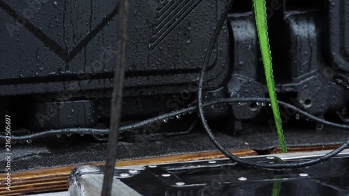 Close-up of wet black electrical panel with green cable under rain. Water droplets on exposed contacts create severe short circuit hazard, potential fire, dangerous outdoor safety risk. 4k video