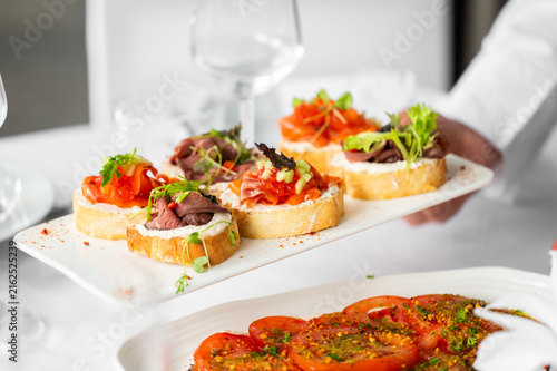 Photography Assorted crostini and bruschetta appetizers served on a white plate by a waiter in a restaurant