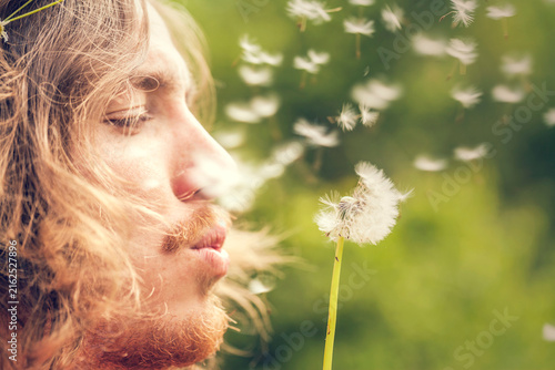 Young man blows a dandelion outdoors