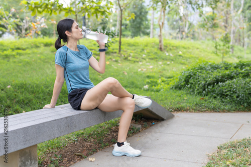 Fotografie woman drinking water after outdoor exercise in green park, staying hydrated during fitness training, running, workout recovery, active lifestyle