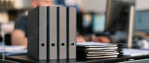 Binder and folder organization on a clean office desk with paper document stack