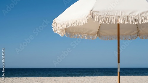 White beach umbrella with fringe standing on tropical sandy shore against blue sea and clear sky umbrella vacation