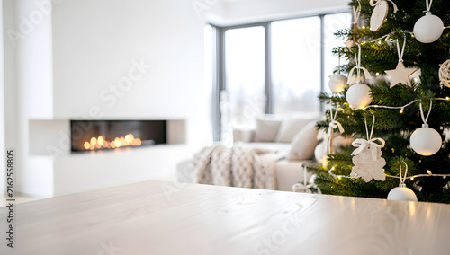 Bright modern minimalist living room featuring a blank white wooden table and an elegant Christmas tree decorated with wooden ornaments
