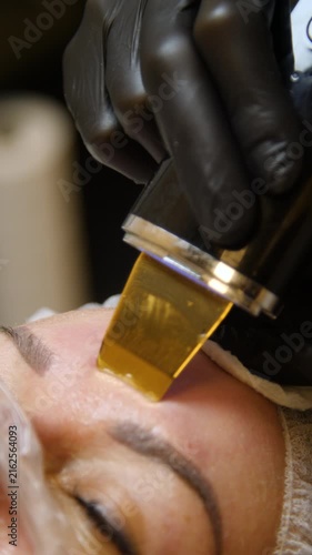 Professional beautician applying cleansing mask on female client's face. Close-up of female face during youth restoration and facial rejuvenation procedure  - Vertical Video
