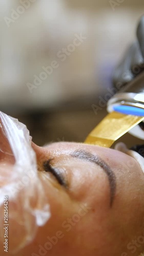 Professional beautician applying cleansing mask on female client's face. Close-up of female face during youth restoration and facial rejuvenation procedure  - Vertical Video