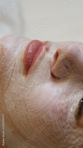Professional beautician applying cleansing mask on female client's face. Close-up of female face during youth restoration and facial rejuvenation procedure  - Vertical Video