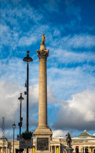 View of Nelson's Column with its statue of Admiral Nelson, ornate capital, and bronze reliefs under a blue sky with clouds in London, England, United Kingdom.