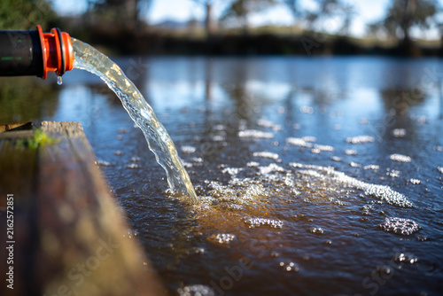 Water pumping from a pipe hose creating bubbles into a farm dam in rural Australia