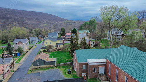Bright green church roof borders Washington Street alongside historic brick houses. Sloping forested mountain ridges frame quiet residential enclave in Harpers Ferry, West Virginia
