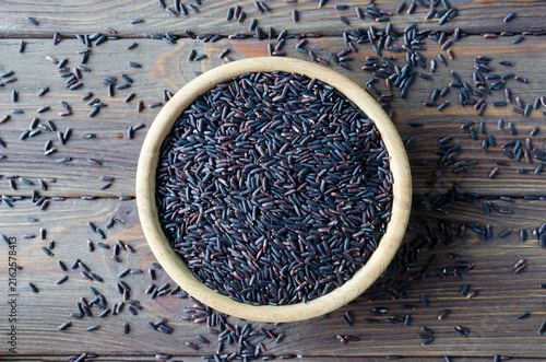 Foto Organic Black Rice in a ceramic bowl with grains scattered around on a wooden table