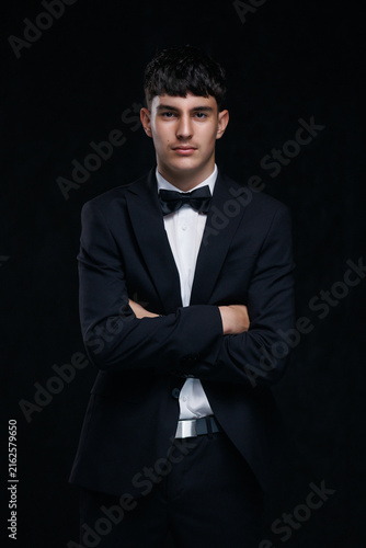 Confident young man in black tuxedo with crossed arms and subtle smile