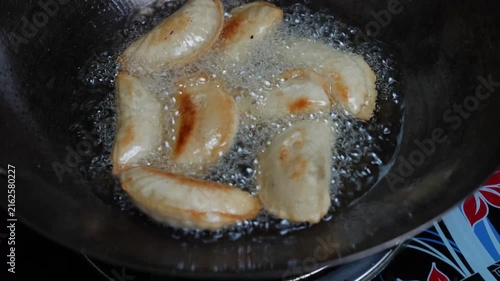 Dumplings frying in hot oil in a pan on a stovetop, with a close-up view of cooking food at home