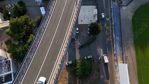 Bridge spans roadway.
Cars cross bridge.
Vehicles navigate intersection.
Houses surround streets.