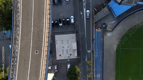 Bridge spans roadway.
Cars cross bridge.
Vehicles navigate intersection.
Houses surround streets.