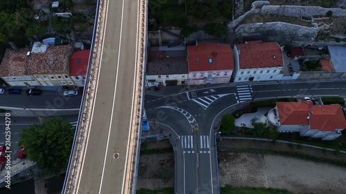 Bridge spans roadway.
Cars cross bridge.
Vehicles navigate intersection.
Houses surround streets.