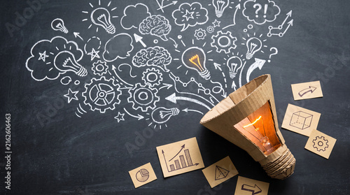 Cardboard lightbulb with glowing filament, surrounded by chalk drawings of ideas, gears, and graphs, symbolizing creativity and innovation
