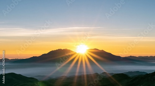 Golden sun rays bursting over layered mountain peaks at dawn, illuminating misty valleys with new light