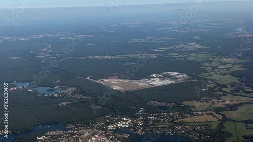 panoramic aerial view - flying along area around Tesla Gigafactory 4, a manufacturing plant for Tesla Inc. located southeast of central Berlin, in Brandenburg, Germany, surrounded by countryside