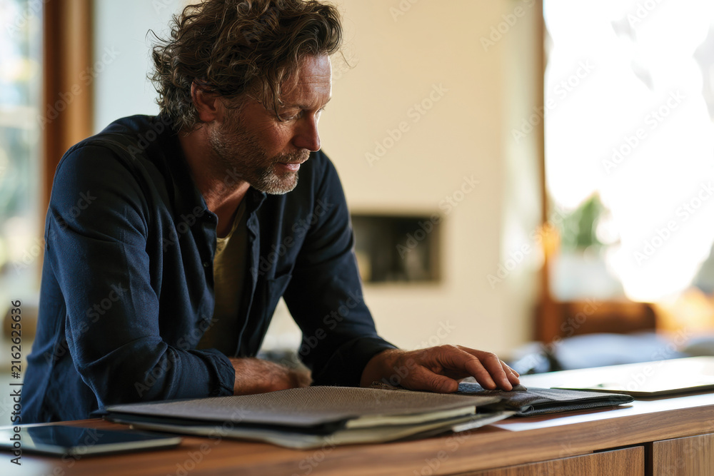Obraz premium A stylish man examines fabric swatches in a bright, modern living space, illustrating creativity and personal style amid an inviting atmosphere filled with natural light.