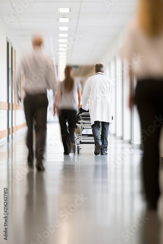 Medical professionals walking down a hospital corridor with a patient on a gurney  viewed from behind.