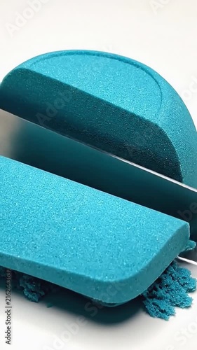 Sharp metal blade cutting through textured blue kinetic sand creating satisfying shapes and crumbs